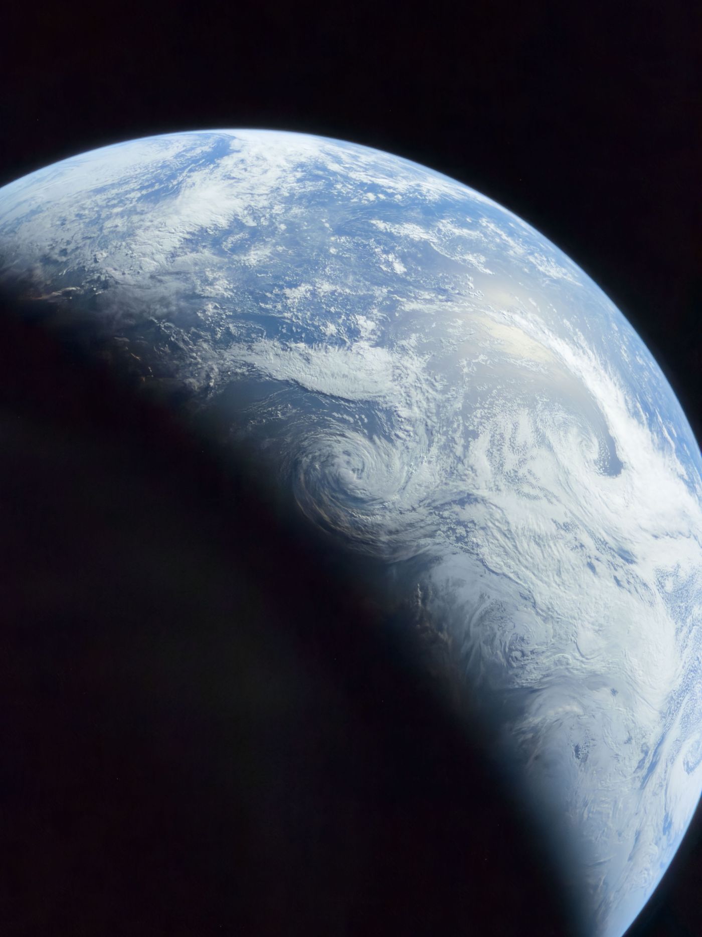 Half-lit Earth with white swirling storm clouds over the deep blue Pacific Ocean, the night side fading into darkness