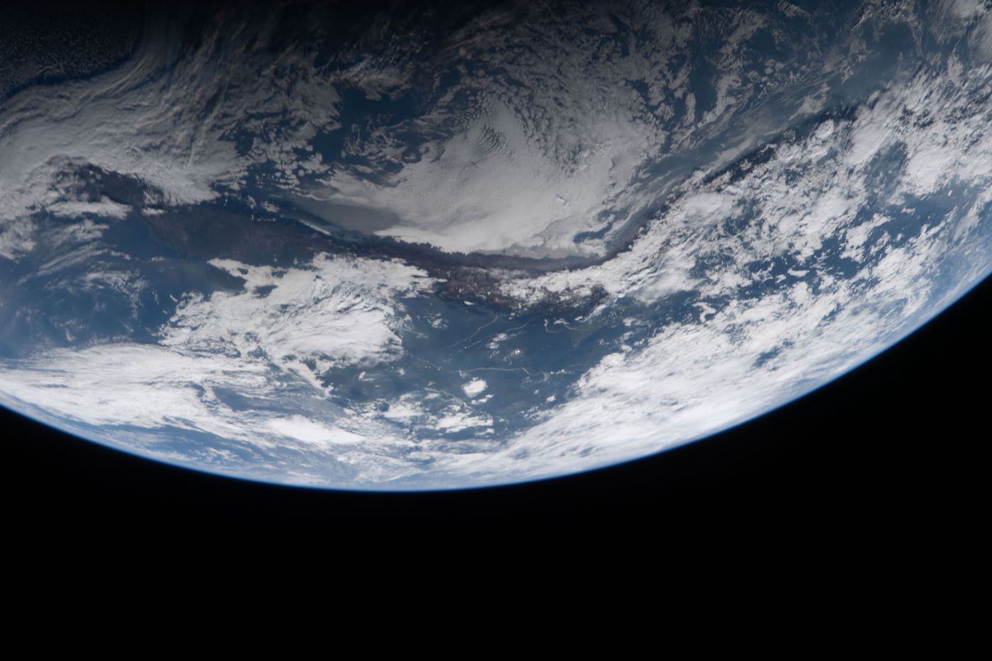 The underside of Earth&rsquo;s globe, blue ocean and bright clouds edged by a thin blue atmosphere against black space